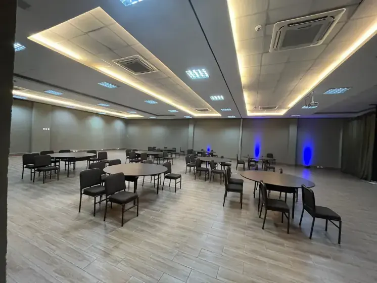 Salão dividido e montado com mesas redondas e iluminação cênica